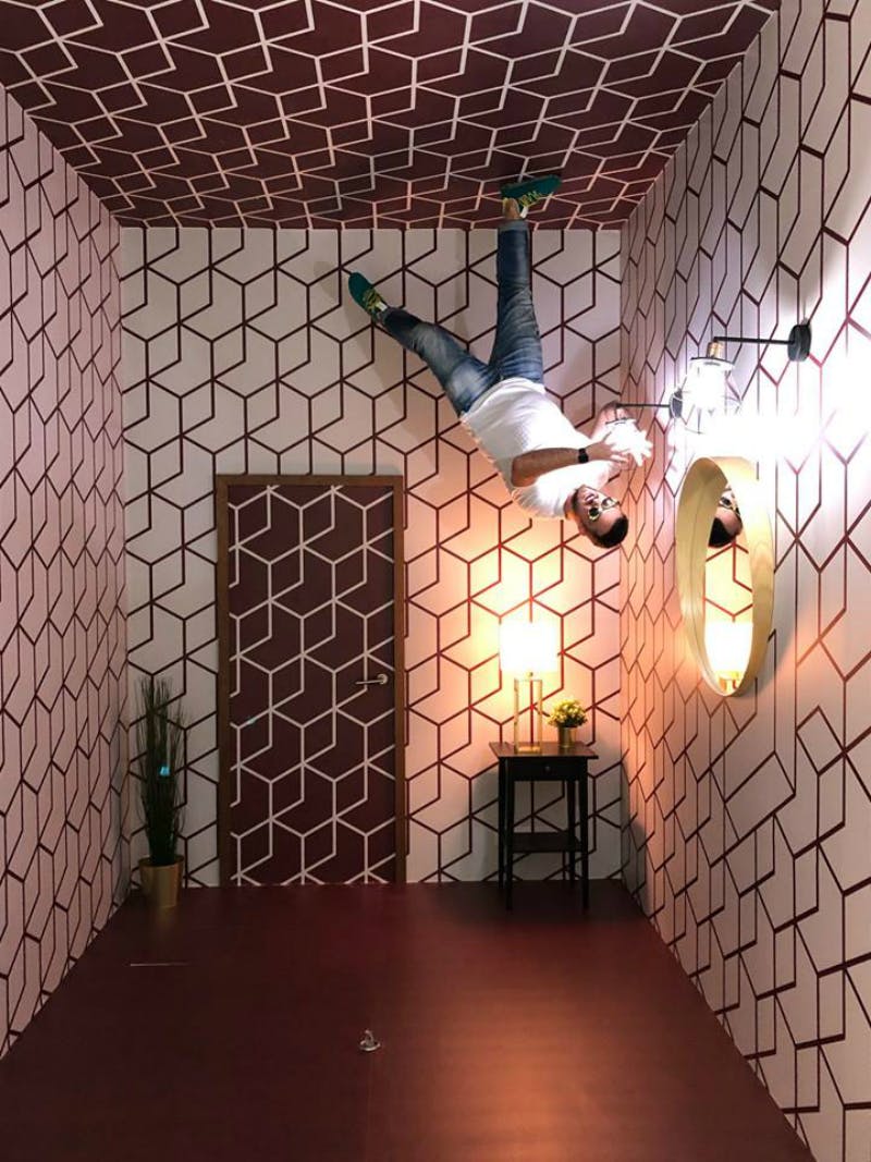 V místnosti s geometrickým vzorem, dveřmi, zrcadlem a lampou, se objeví muž vzhůru nohama, který se zdánlivě prochází po stropě.