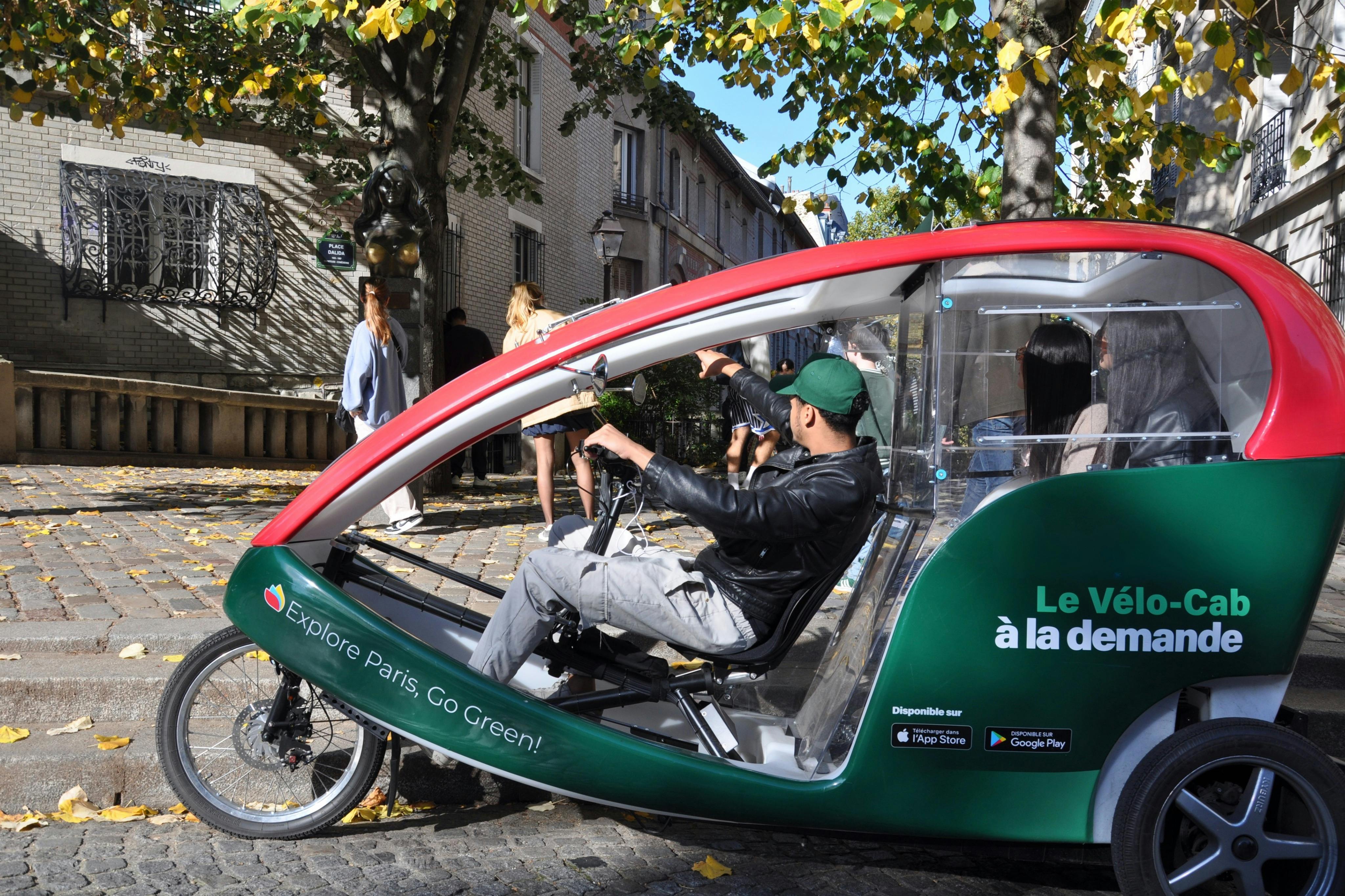 Person riding a green and red pedicab with "Explore Paris. Go Green!" written on the side, on a tree-lined street.