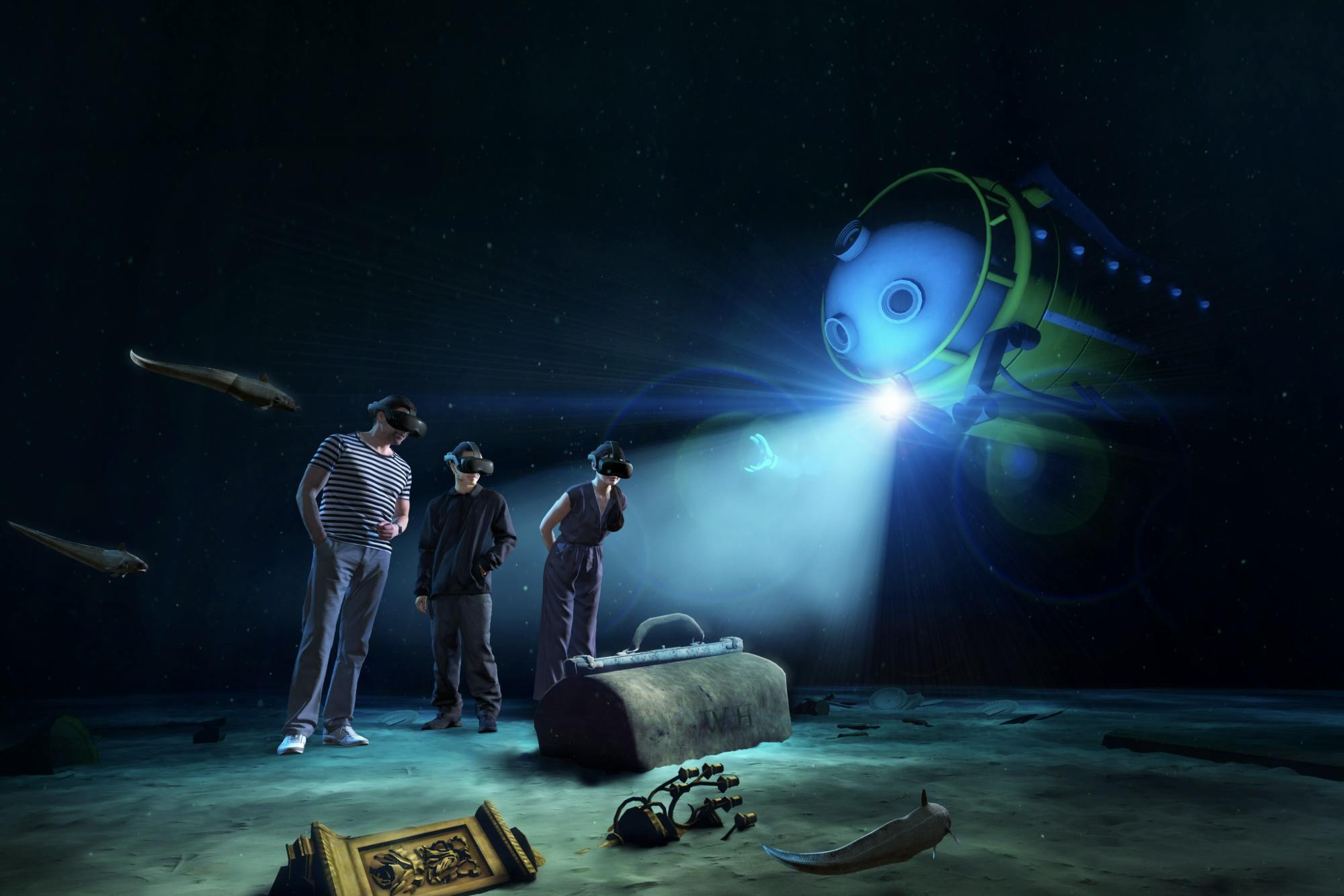 Trois personnes portant des casques de réalité virtuelle explorent une scène sous-marine avec des raies, un coffre au trésor et un submersible robotisé.