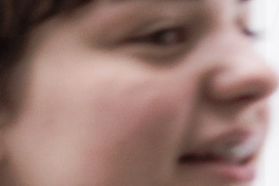 A young person in a denim jacket smiles in the foreground, with a modern building interior and people in the background.