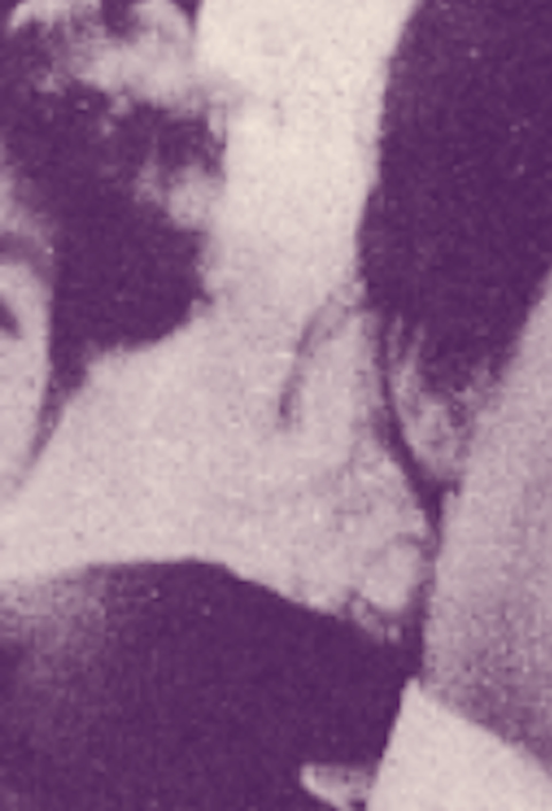 A person is wrapped in a long, dark, draped fabric with their face visible at the top, looking upwards.
