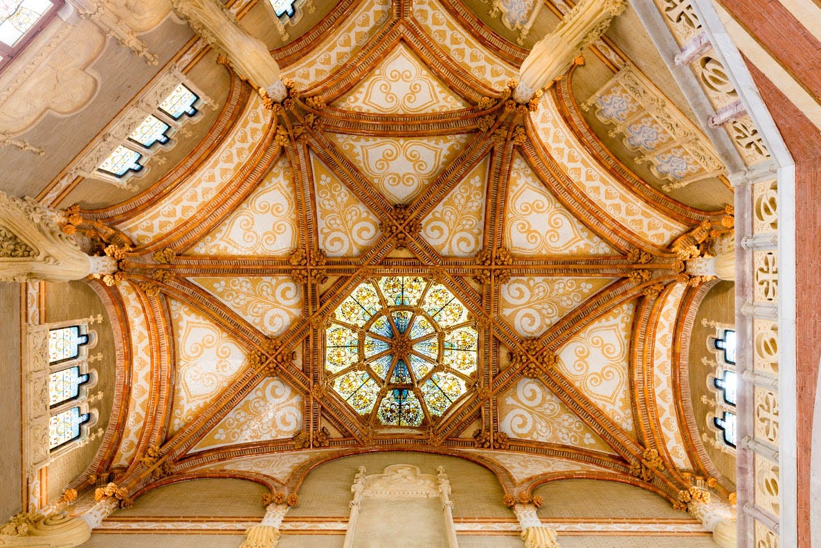 Ornate ceiling with intricate golden patterns, arches, and a central stained glass skylight. Architectural and decorative details.