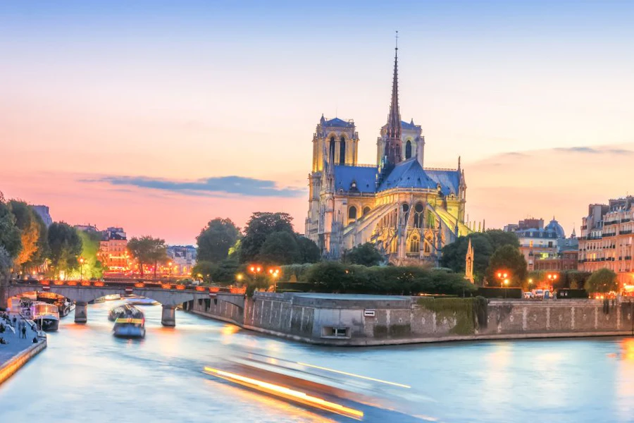 Notre-Dame Cathedral at sunset, seen from across the river with city lights beginning to glow
