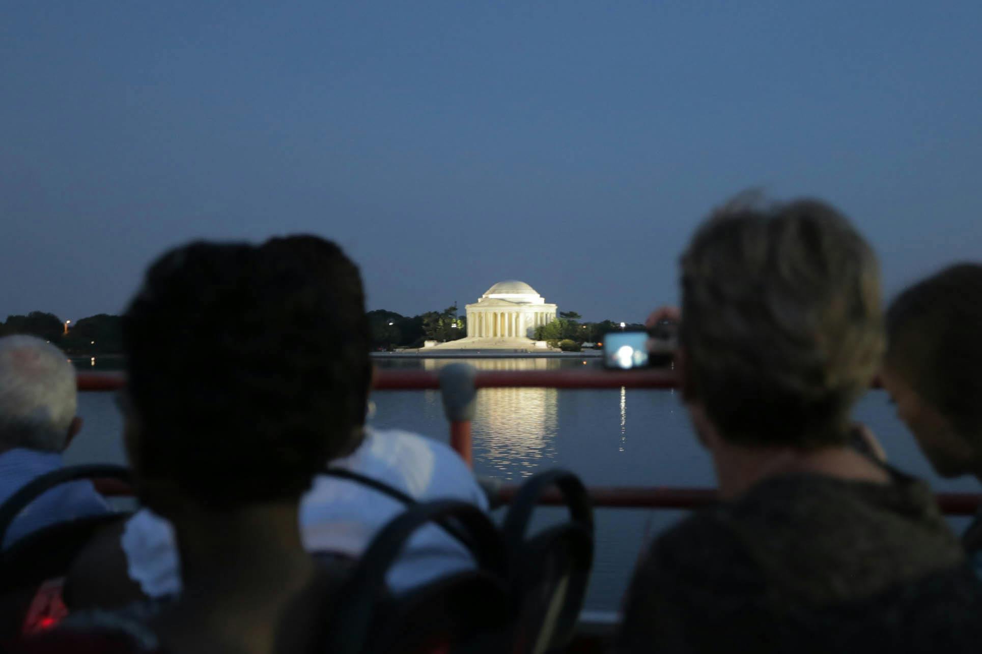 해질 무렵 보트를 탄 두 사람이 조명이 켜진 제퍼슨 기념관을 바라보고 있으며, 한 사람이 카메라에 장면을 포착하고 있습니다.