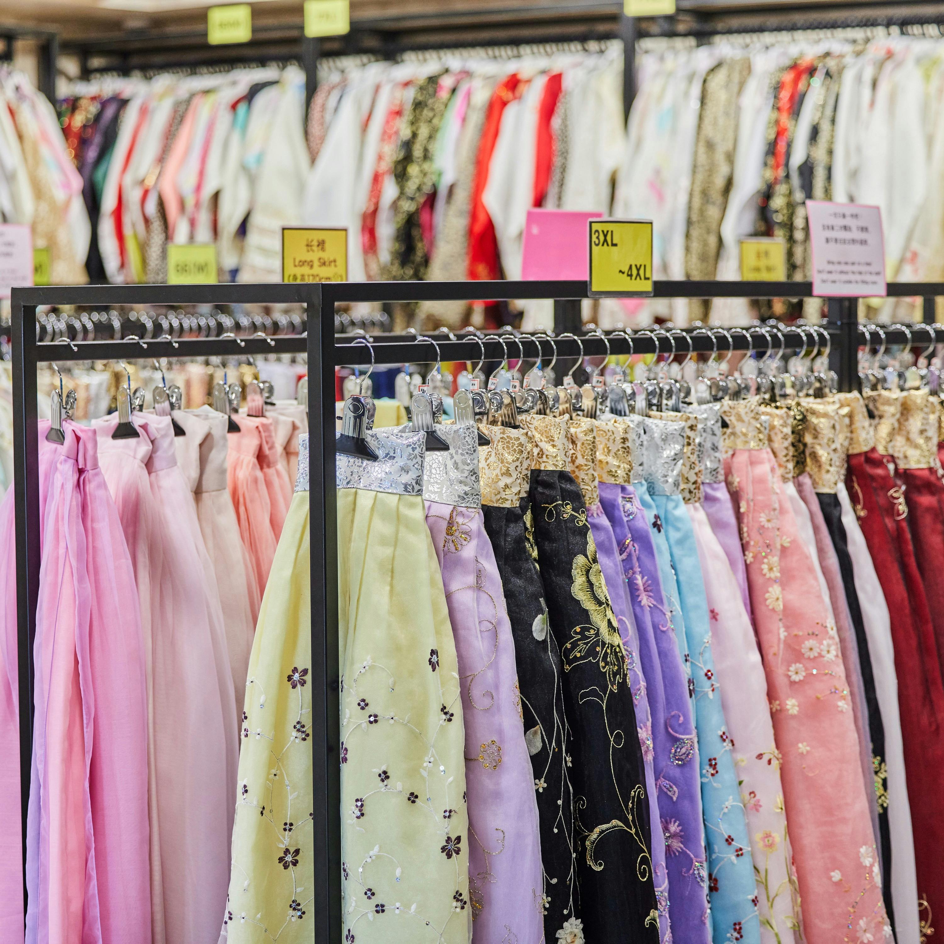 A clothing store displaying rows of colorful traditional dresses on racks, arranged by size with visible labels.