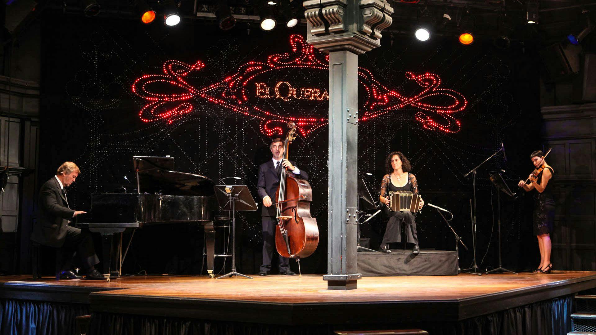 Musicians perform on a stage, one playing a double bass and the other a bandoneon, with "El Querandi" in red lights behind them.