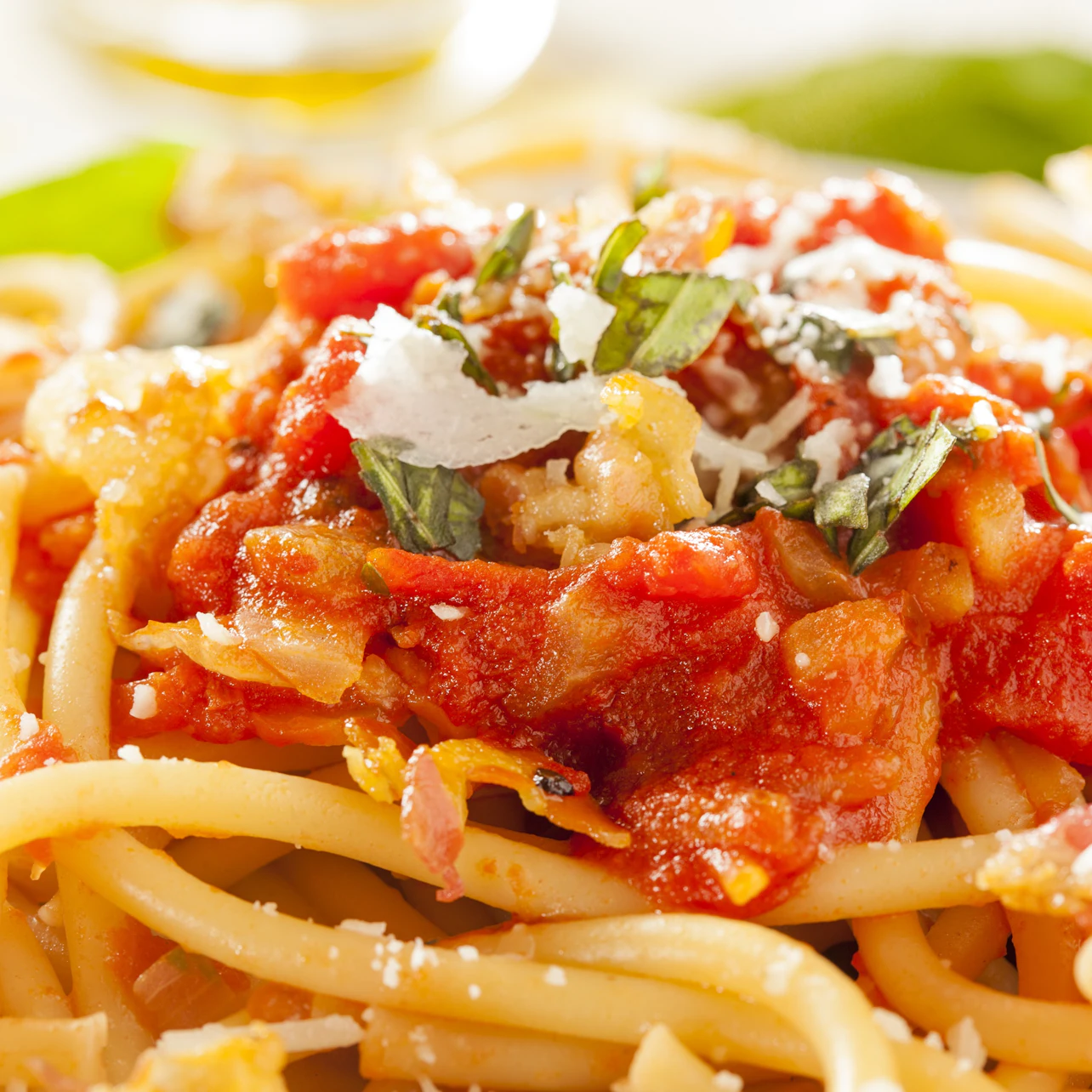Close-up of pasta with tomato sauce, grated cheese, and fresh basil leaves.