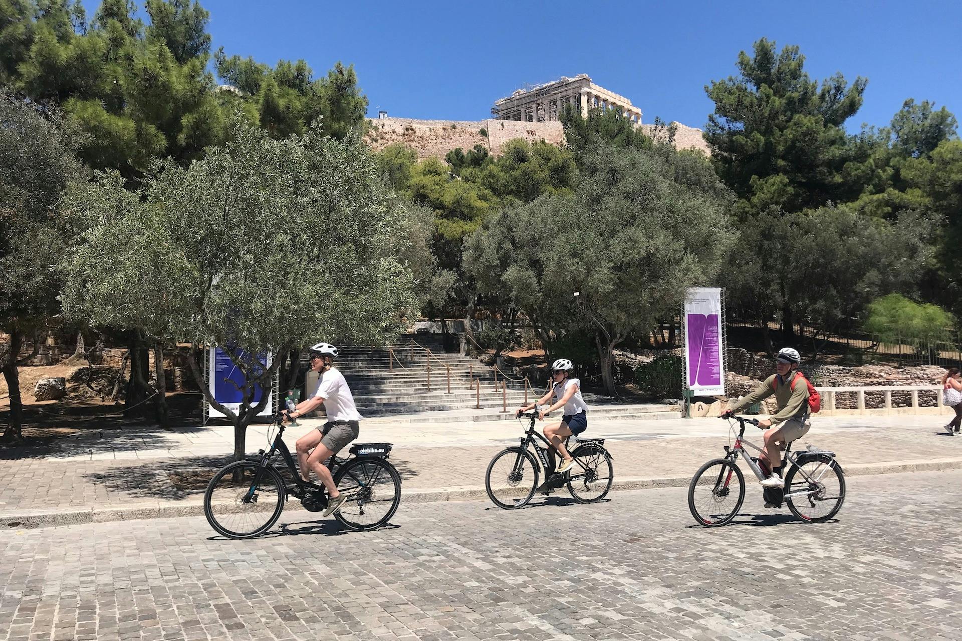 Tre ryttere, der cykler med elcykler under Parthenon