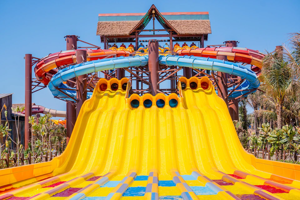 A brightly colored water slide structure with multiple yellow chutes and blue and red tubes under a clear blue sky.