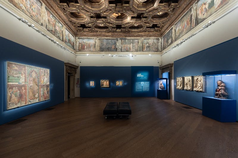 Una galleria d'arte con pavimenti in legno, soffitto decorato, affreschi alle pareti e sculture astratte nere su pareti bianche.