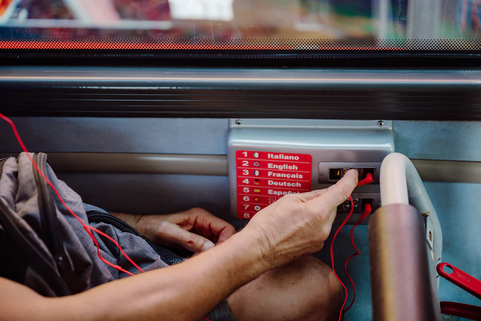 A person is selecting a language option on an audio guide device, with red cables connected to it.