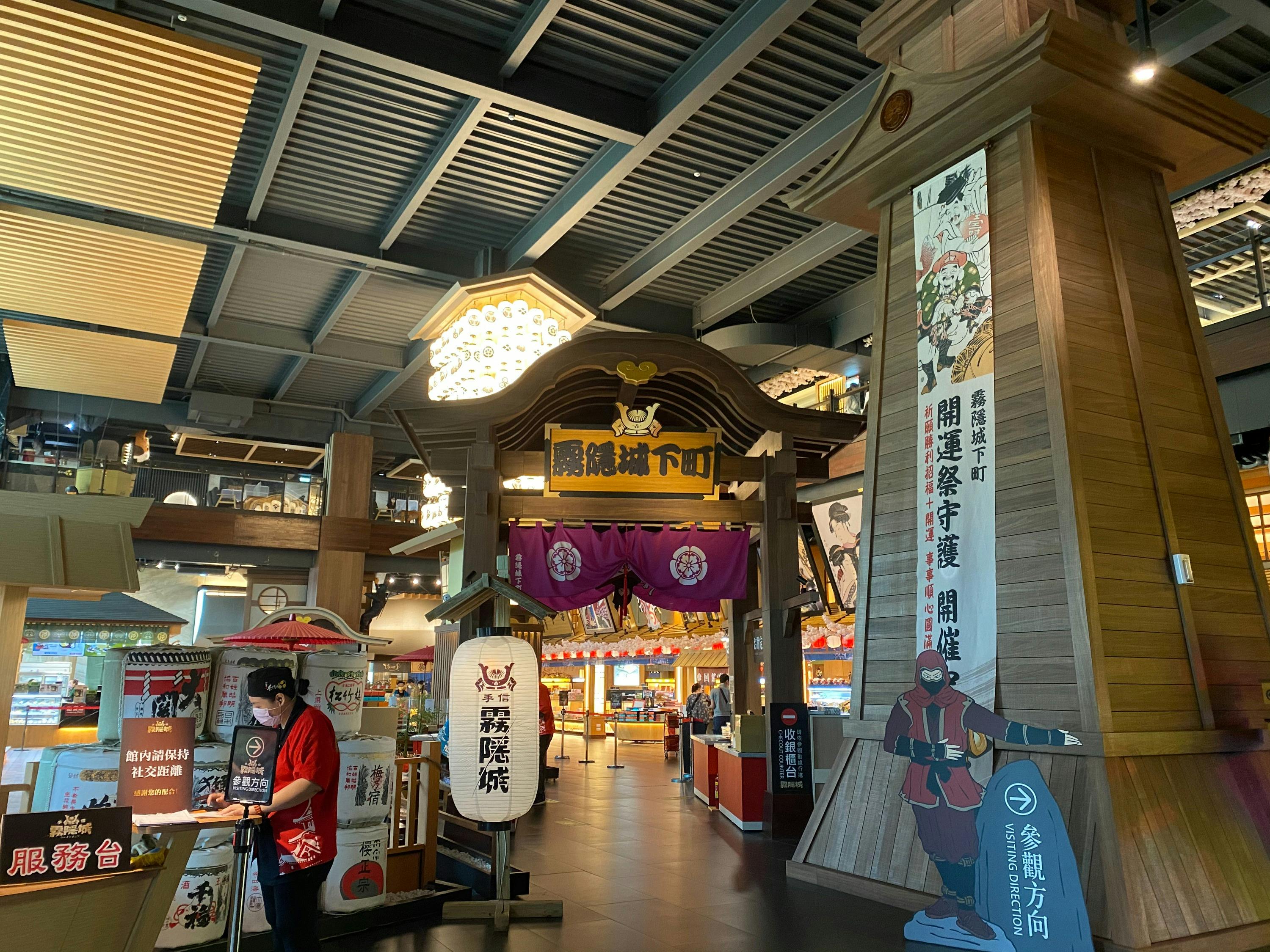 Indoor market area with a traditional Japanese-style entrance, colorful banners, and a person standing near a stall.