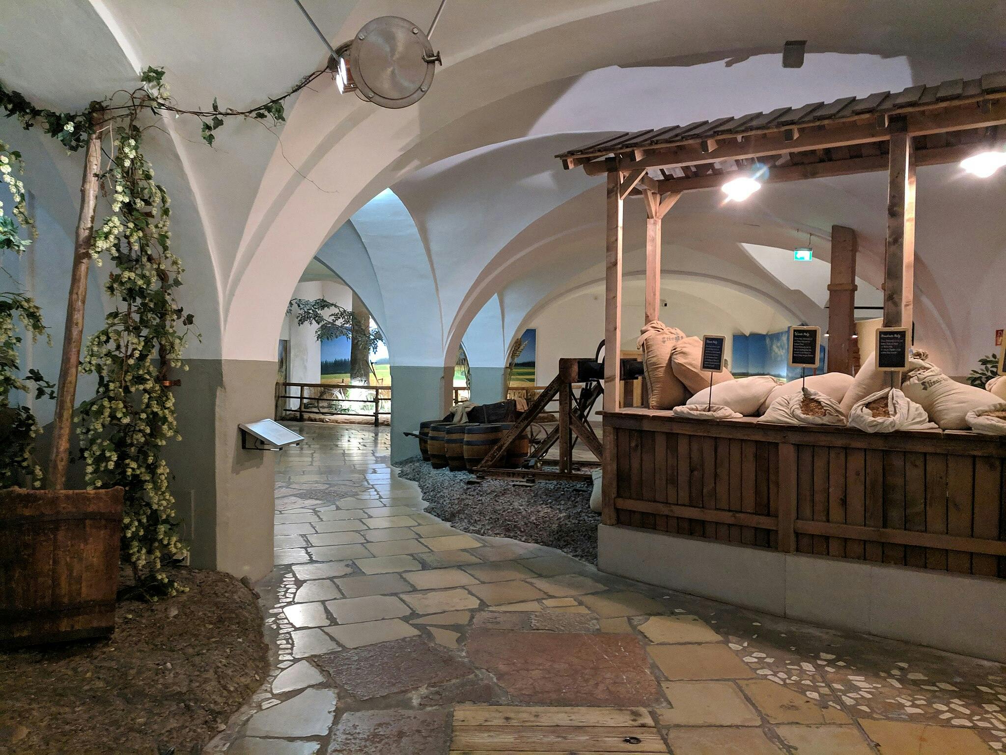 Крытый рынок с арочными потолками, деревянными киосками, мешками с продуктами, зеленью и вымощенной камнем дорожкой.