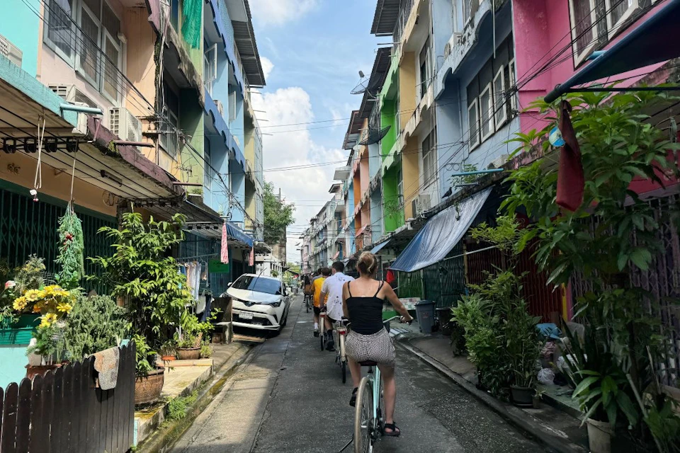 Cyclists riding past vibrant homes in a Bangkok backstreet community