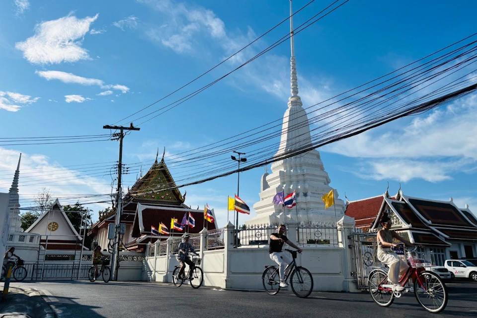 Cyclists riding by a white stupa and temple on a Bangkok bike tour