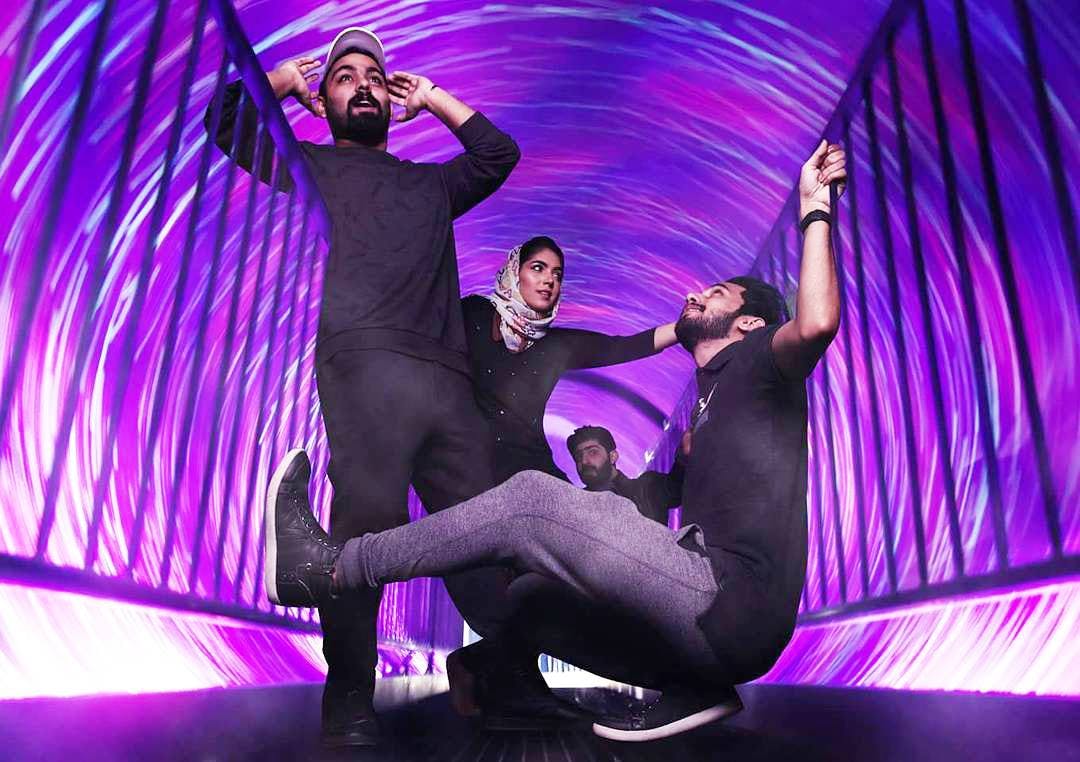 Čtyři lidé jsou uvnitř tunelu s vířícími fialovými a růžovými světly a dělají animovaná gesta a pózy.