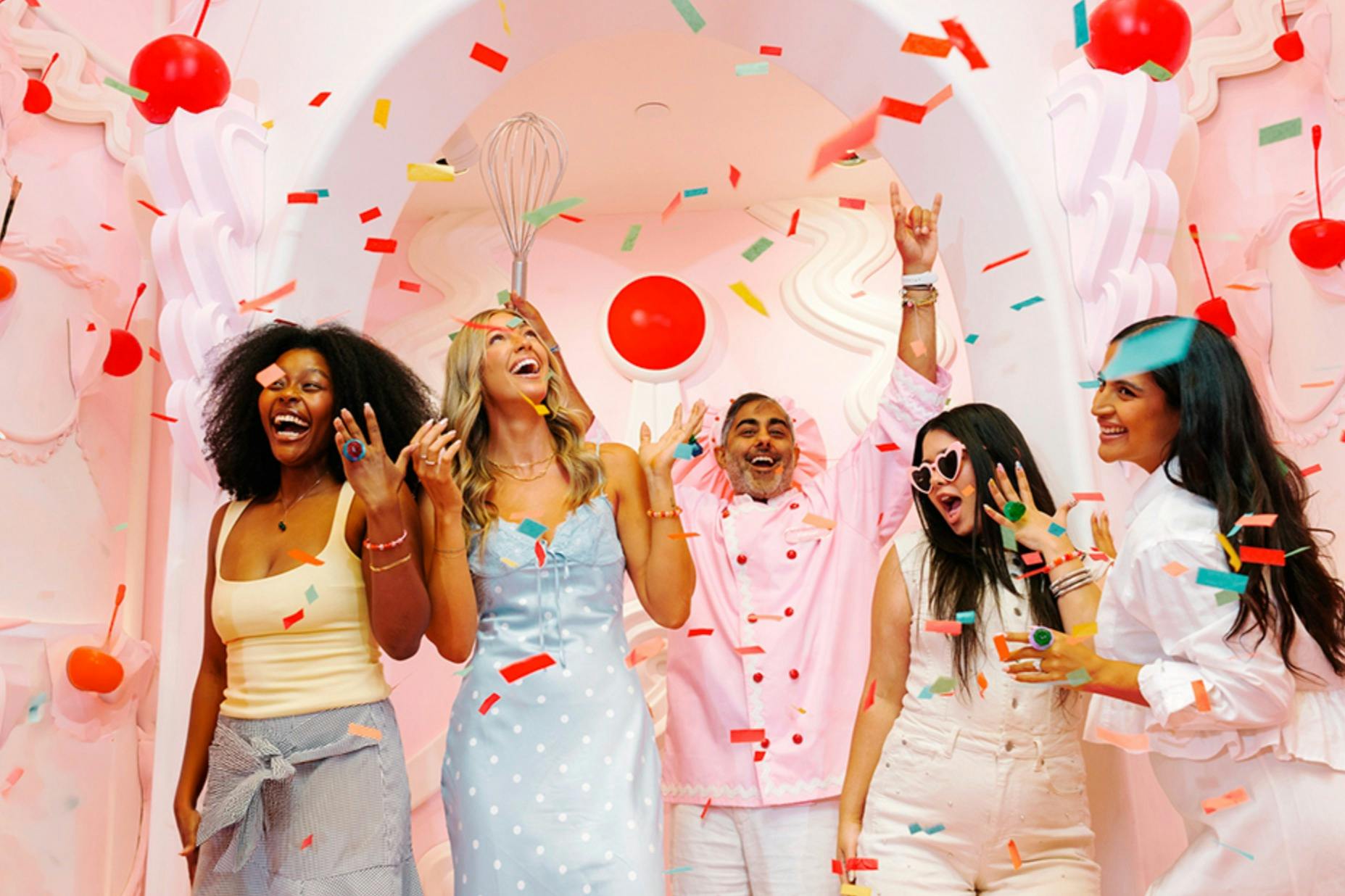 Three people celebrating under falling confetti in a colorful, festive setting.