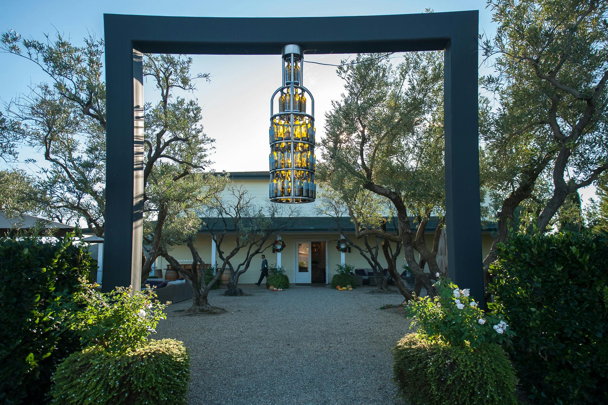 木々や茂みに囲まれた、吊り下げ式の彫刻が施された中庭入り口は、屋根付きの通路がある建物に通じています。