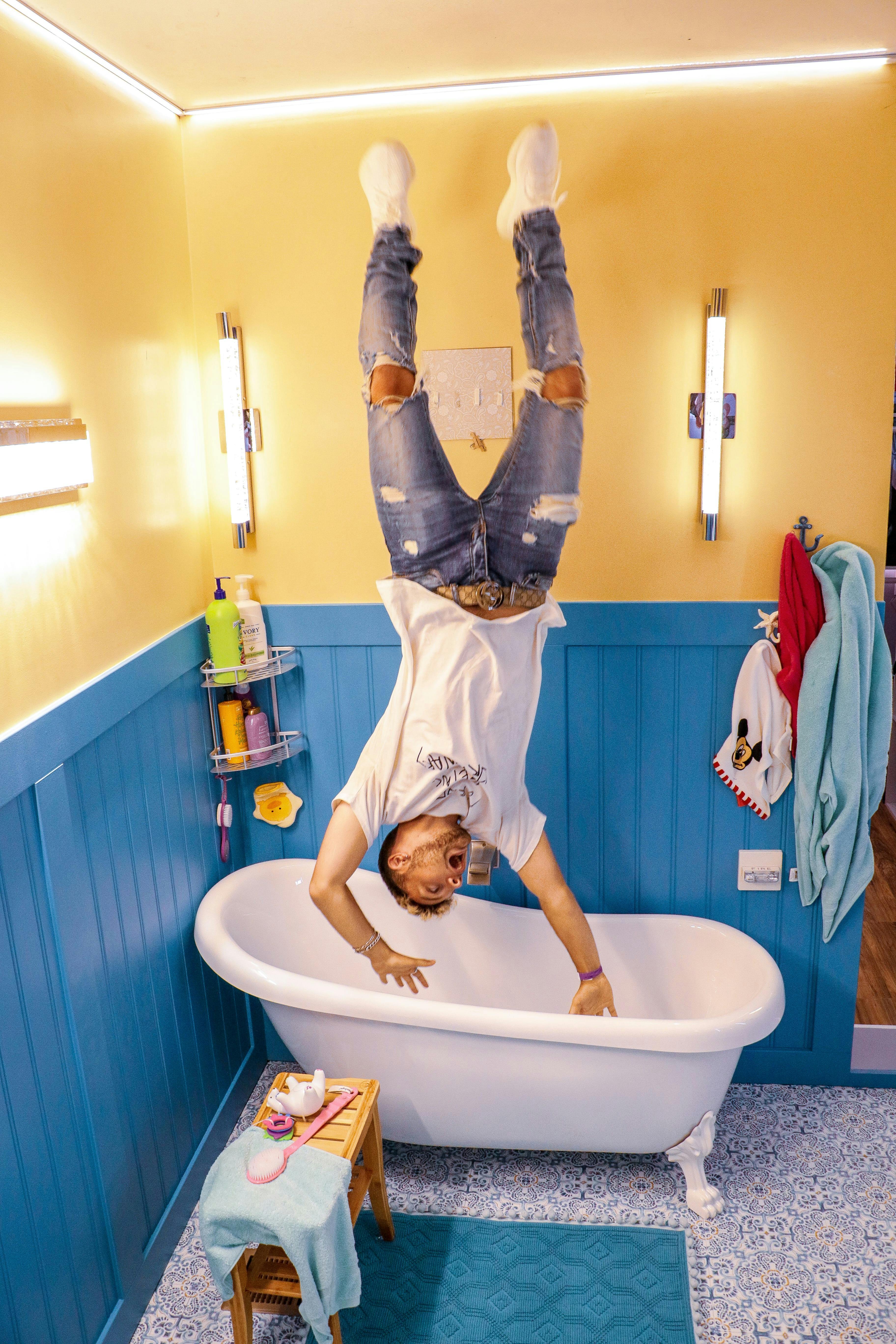Person doing a handstand in a bathroom, with blue paneling and a white bathtub. Accessories and towels are on the walls.