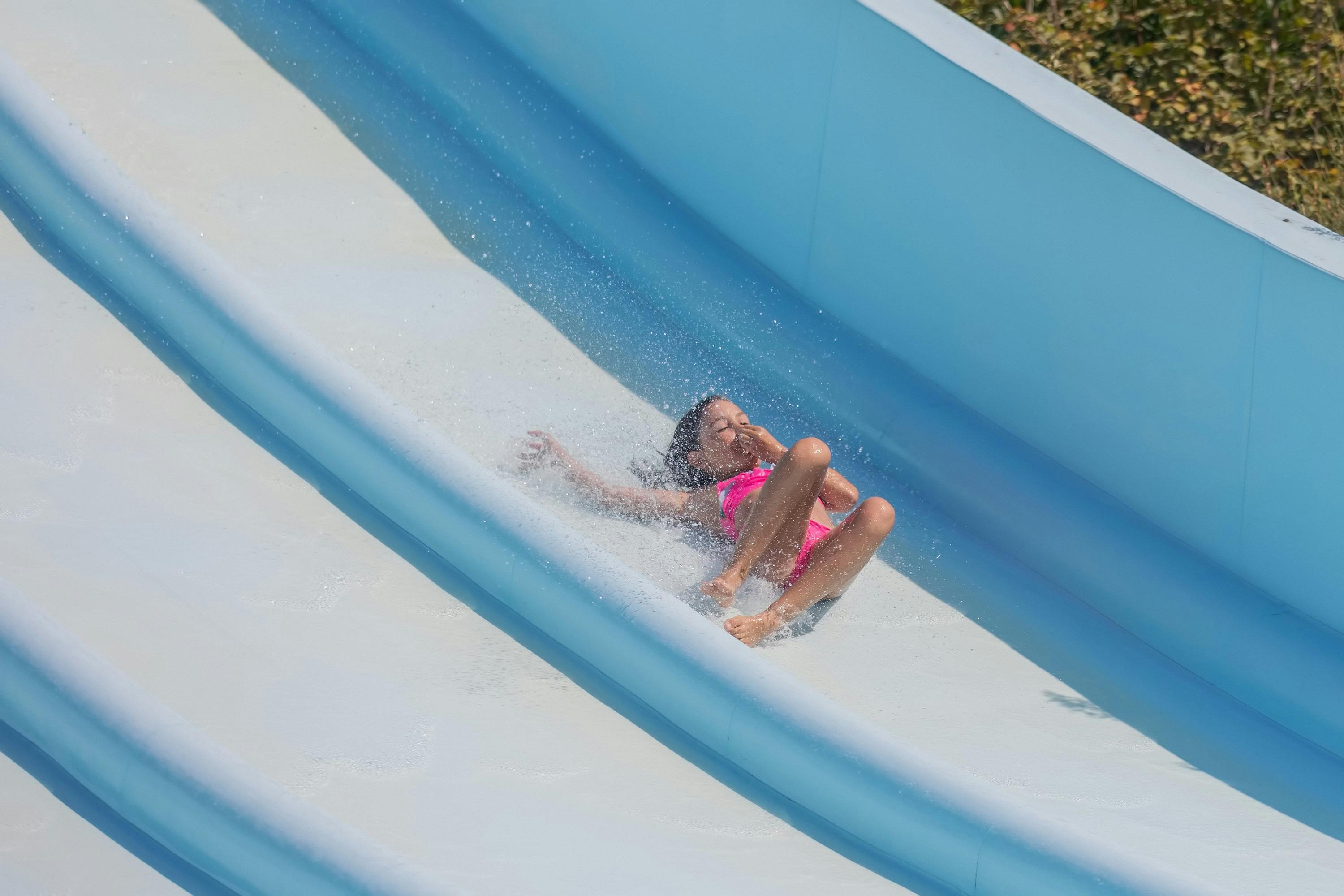 Eine Person in einem rosafarbenen Badeanzug rutscht eine blaue Wasserrutsche hinunter, während das Wasser umherspritzt.