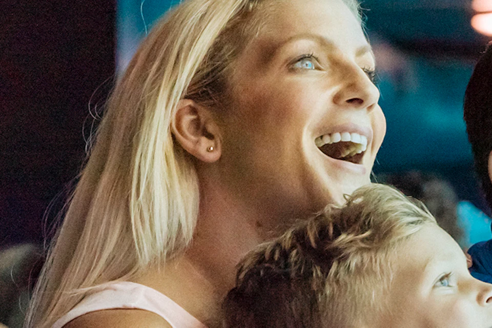 A family excitedly watches marine life through an aquarium window, with other visitors observing in the background.