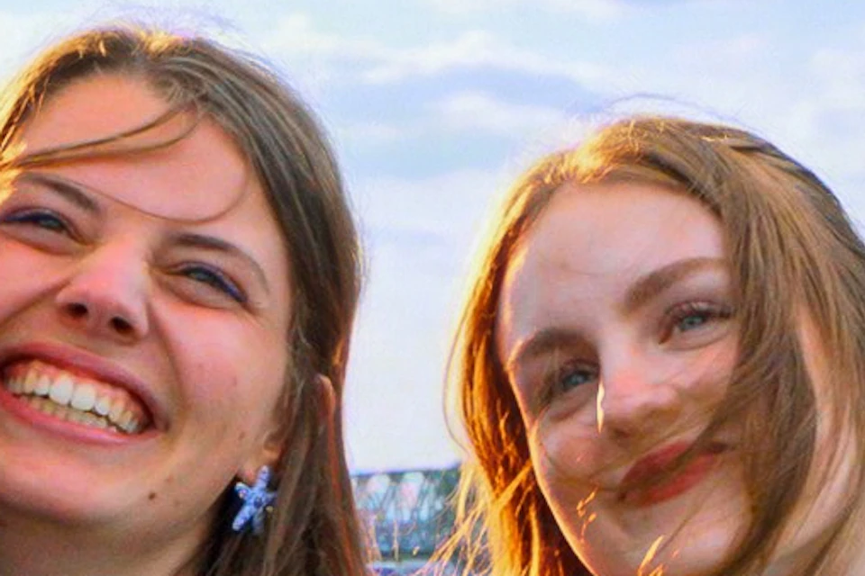 A group of four people smiling and taking a selfie on a waterfront promenade with buildings and water in the background.