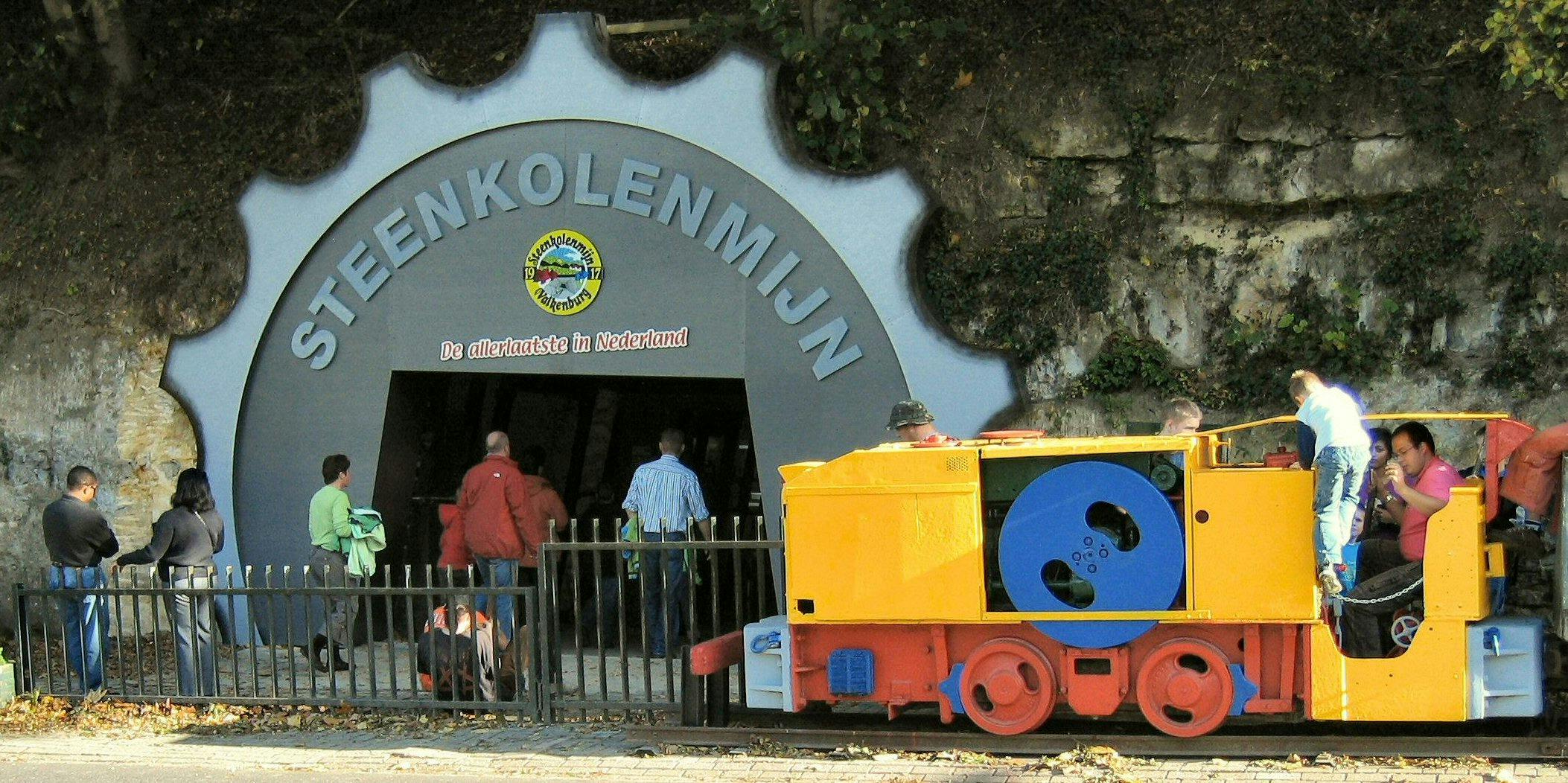 Colorful yellow, red, and blue mini train with people on board, set against a rocky background with vegetation.