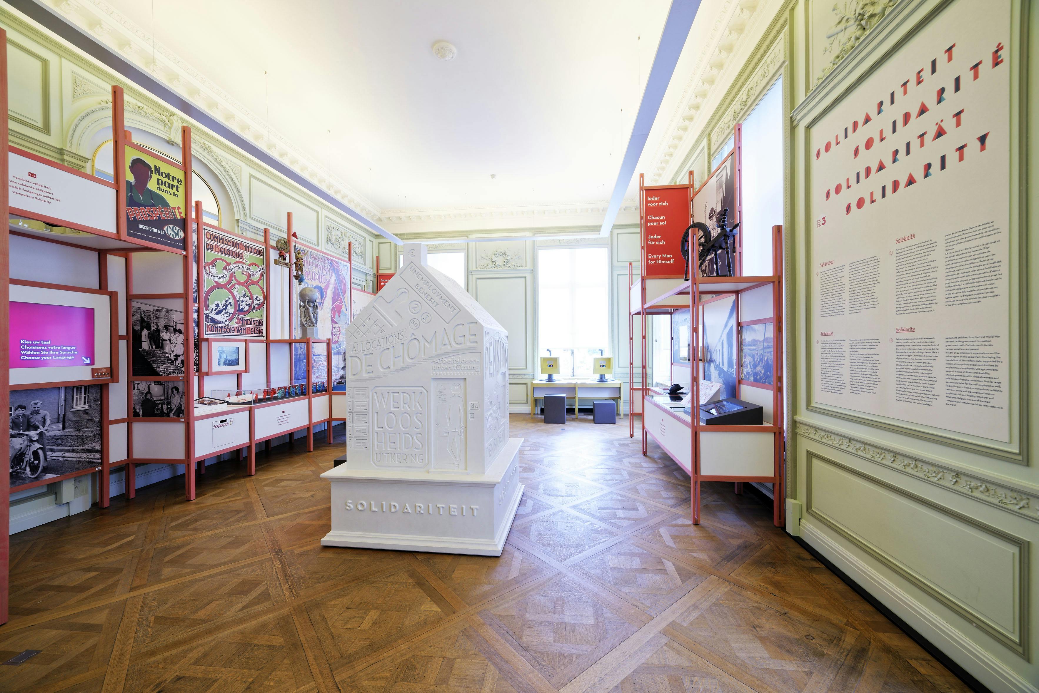 Una exposició del museu presenta una gran escultura de casa blanca amb &#34;SOLIDARITEIT&#34; a la base, envoltada de mostres informatives.