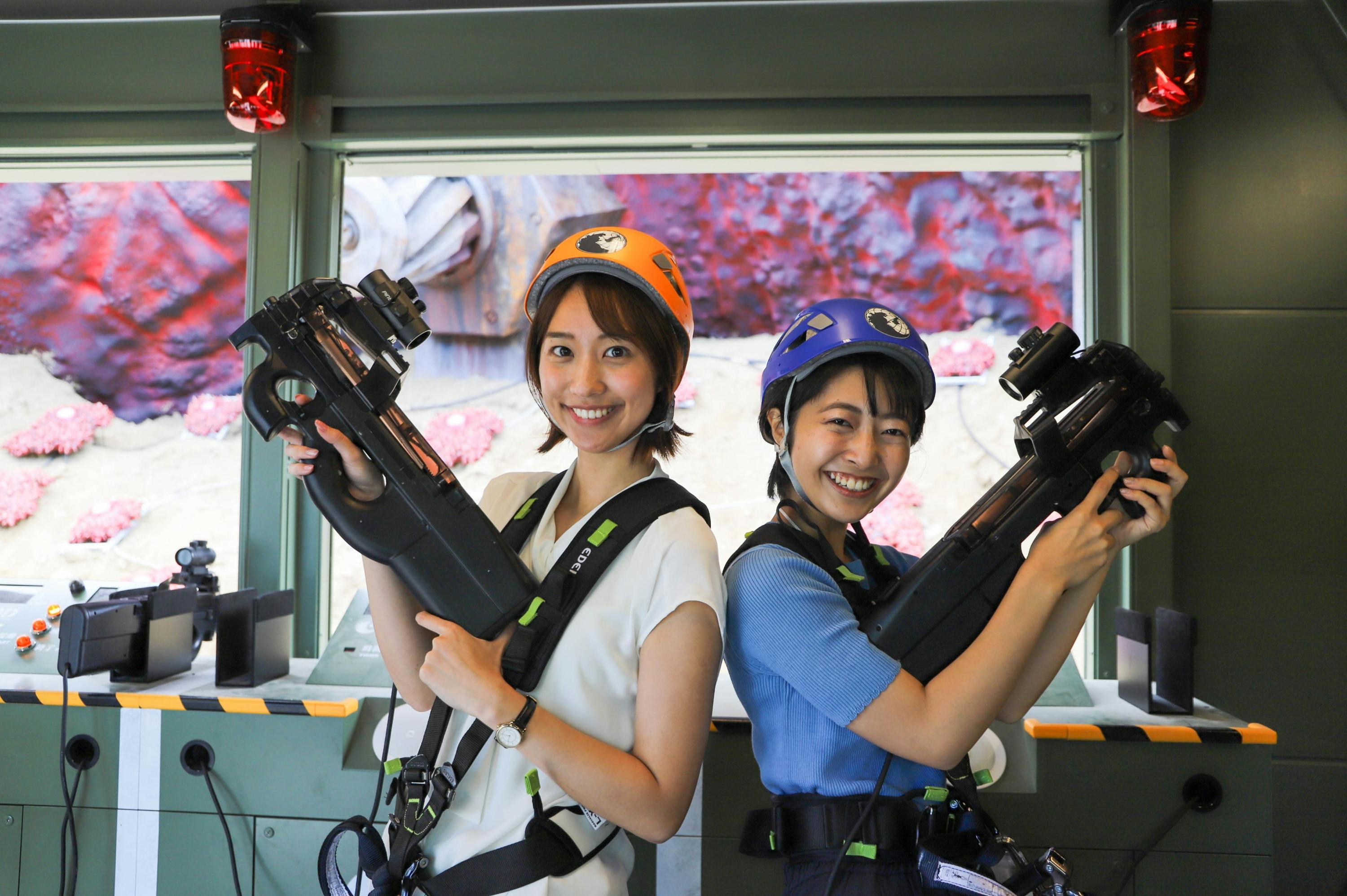 Two smiling individuals wearing helmets and harnesses, holding laser tag guns, standing in a brightly lit room.