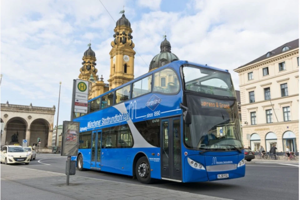 A blue double-decker tour bus is parked in front of a historic building with twin towers.