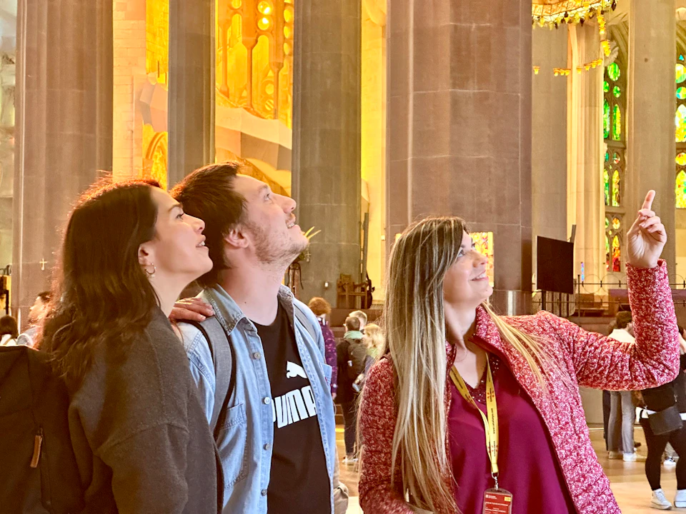 Three people look upwards in awe inside a grand building with tall columns and ornate golden decorations.