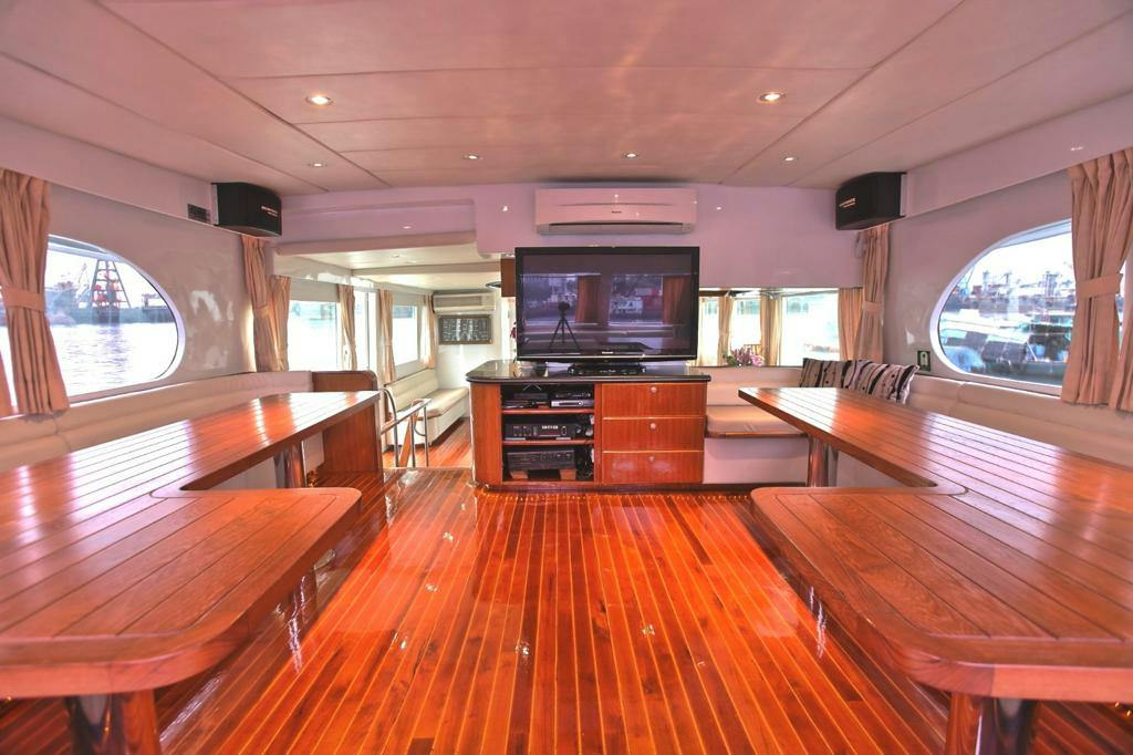 Interior of a yacht with polished wood flooring, dining tables, a television, and seating areas under recessed lighting.