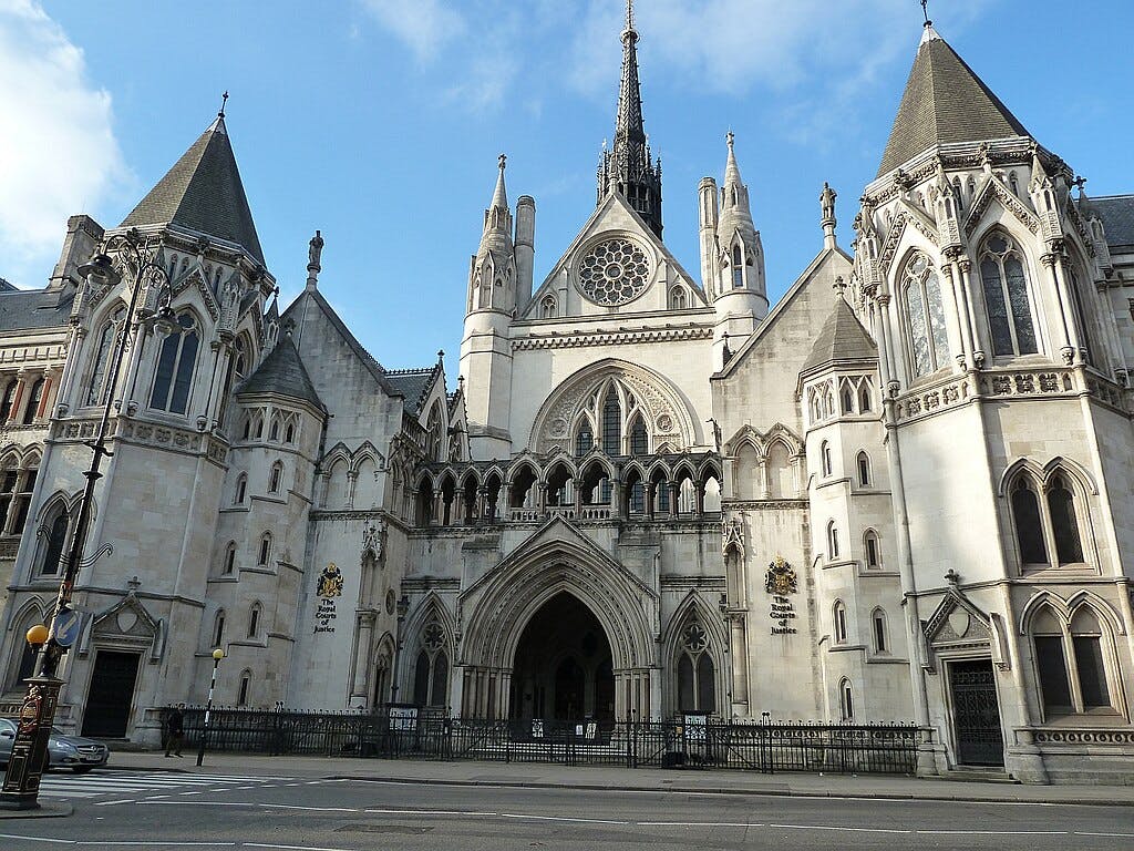 Palais de justice de style gothique avec des arcs en ogive, de hautes flèches et des sculptures ornementales sous un ciel bleu, identifié comme "The Royal Courts of Justice".
