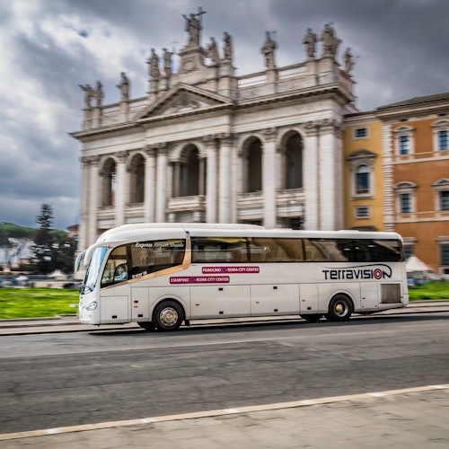 A white Teravision tour bus passes by an ornate, historic building with columns and statues under a cloudy sky.