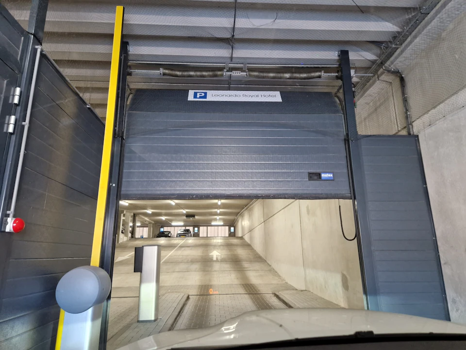 Underground parking entrance with a partially open shutter at Leonardo Royal Hotel, showing a ramp leading to parked cars inside.
