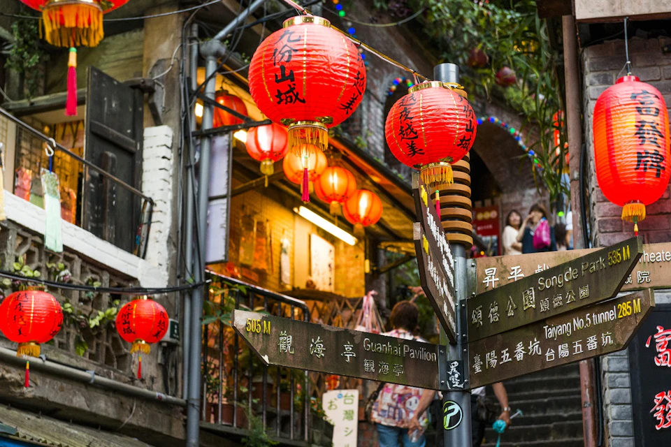 A vibrant street scene with red lanterns, directional signs, and a bustling market atmosphere.