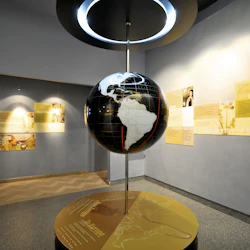 En upphängd jordglob i en museiutställning, omgiven av informativa gula paneler på väggarna.