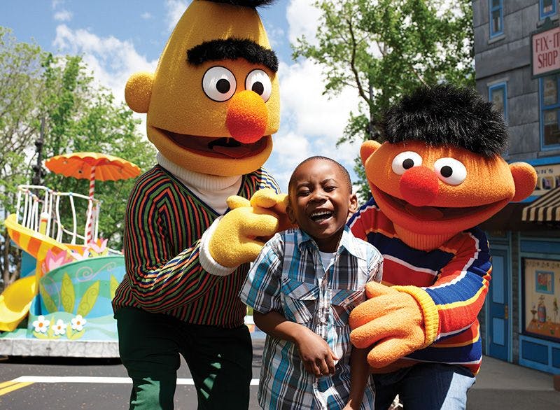 一个孩子微笑着摆姿势，在阳光明媚的日子里，两个角色扮成大黄色木偶和橙色木偶在户外。