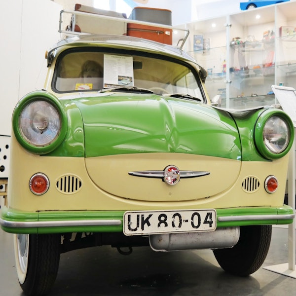 Vintagegrøn og cremefarvet bil udstillet på et museum med nummerplade "UK 80-04" og forskellige artefakter i baggrunden.