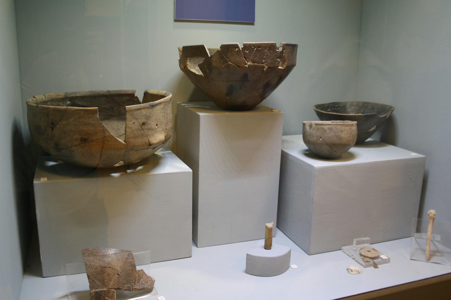 陈列柜展示古老的破碎粘土碗和白色底座上的破碎陶器。