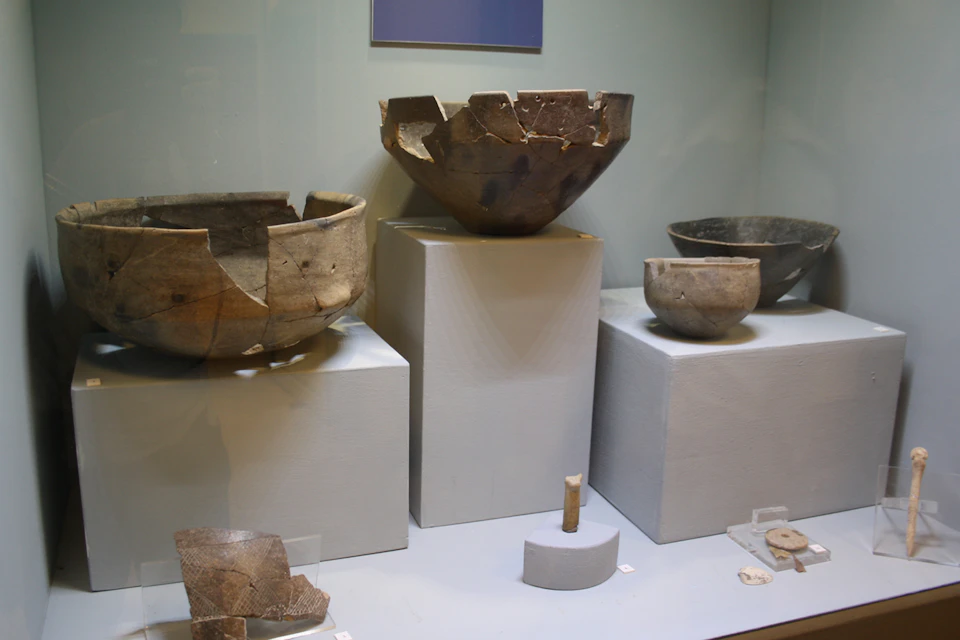 Display case showcasing ancient, cracked clay bowls and broken pottery on white pedestals.
