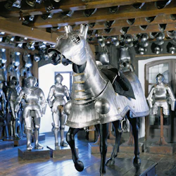 Rummet är fyllt med medeltida rustningar, inklusive flera rustningar och en bepansrad häst som visas upp.