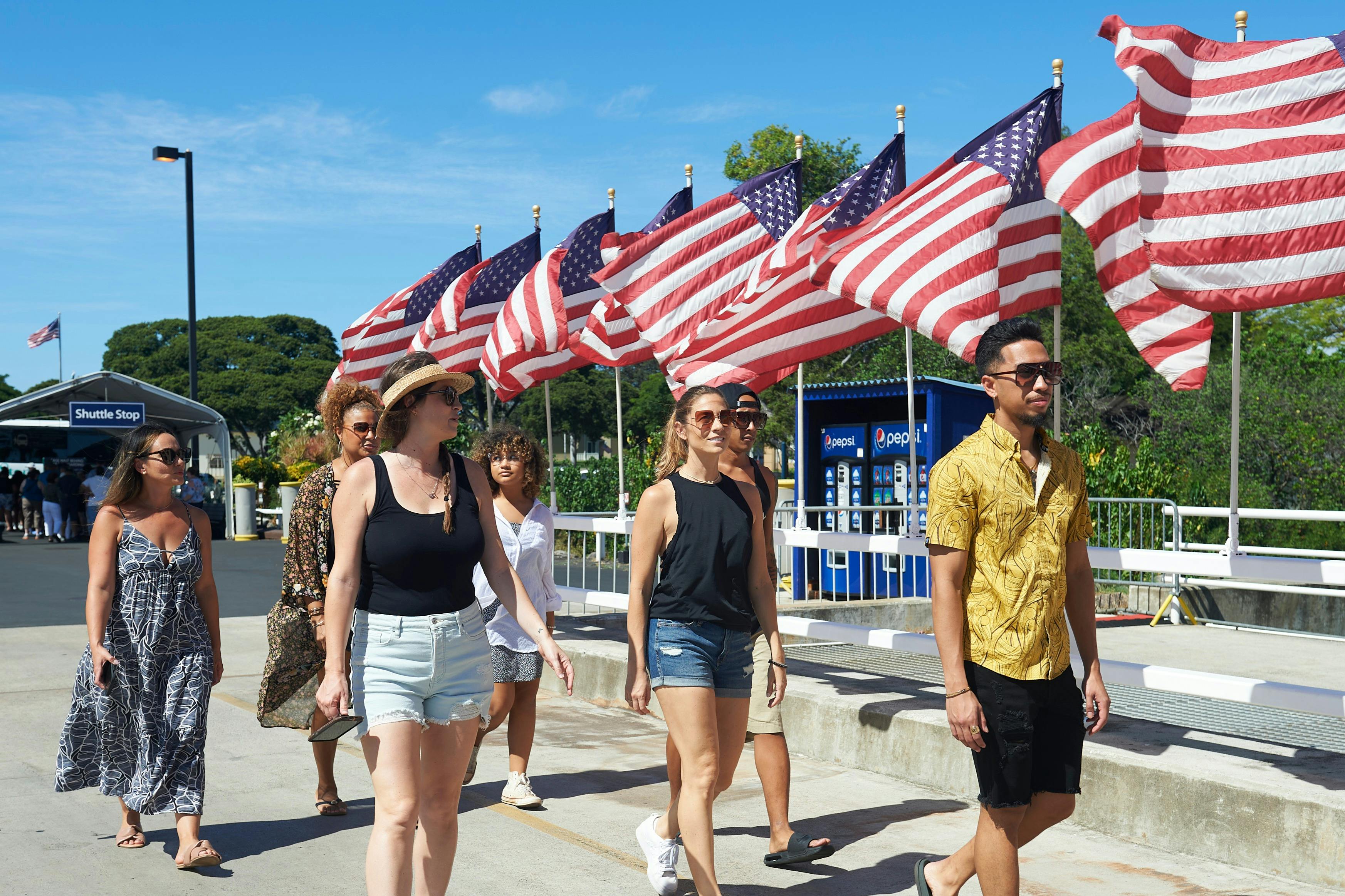 A group of people walking past a row of American flags on a sunny day.