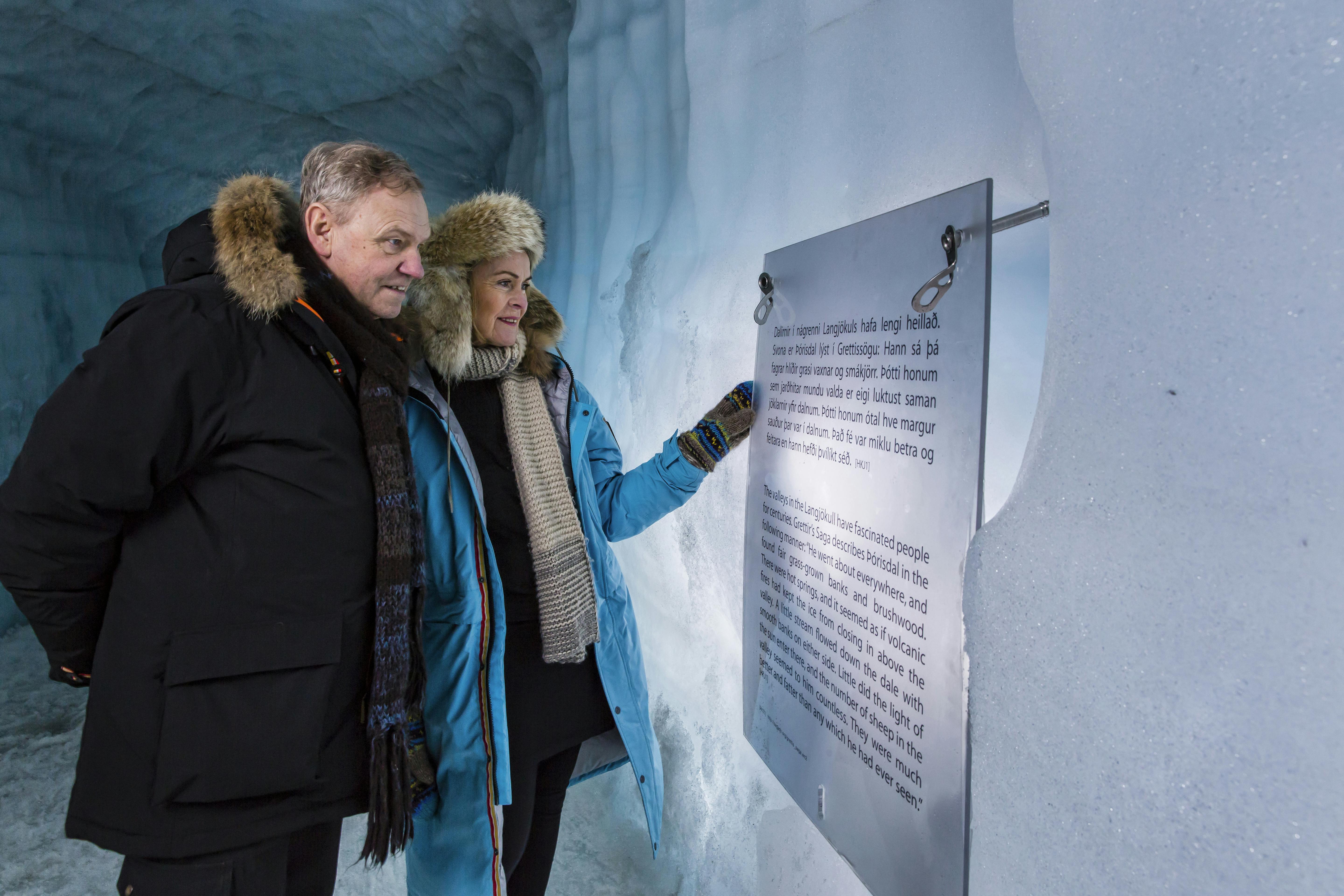 两个穿着冬装的人在冰洞里看到一块牌匾。