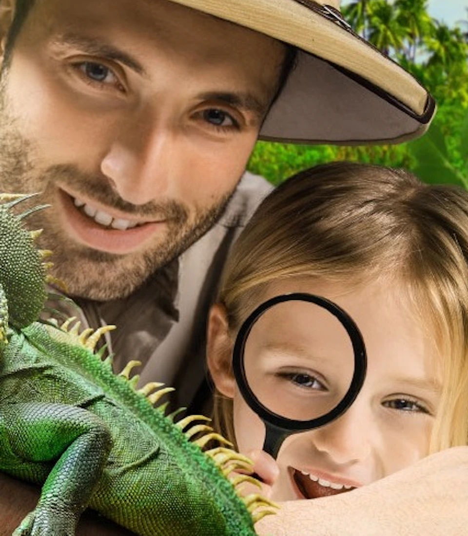 A man and a girl with a magnifying glass observe a green iguana in a lush, leafy environment.