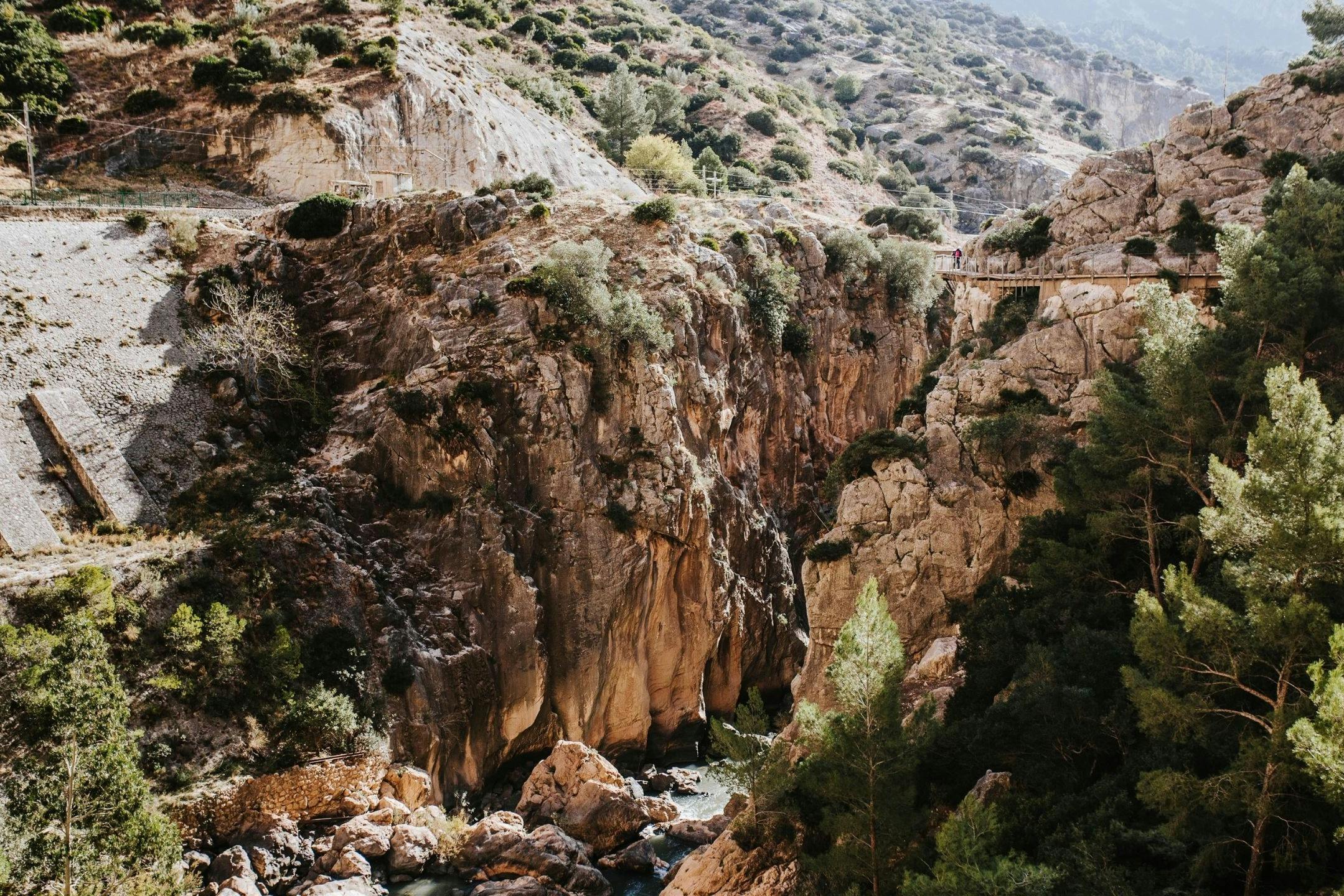 A scenic view of a rocky canyon with a pedestrian walkway along its edge and sparse vegetation on the steep cliffs.