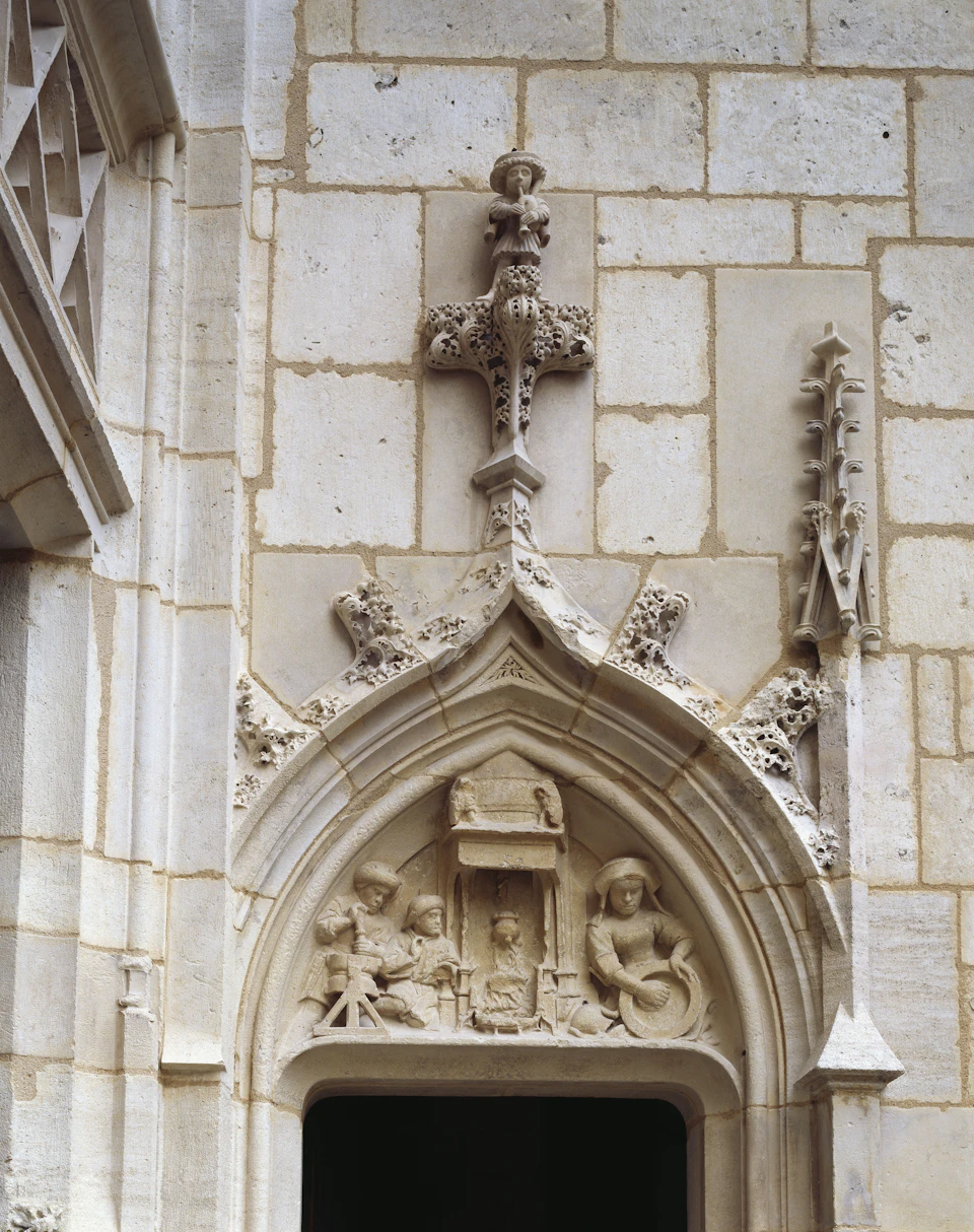 Ornate stone archway with religious carvings depicting figures in a seated position, detailed cross above.