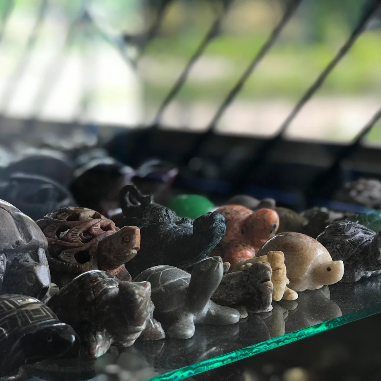 A collection of small turtle figurines made from various materials displayed on a glass shelf.