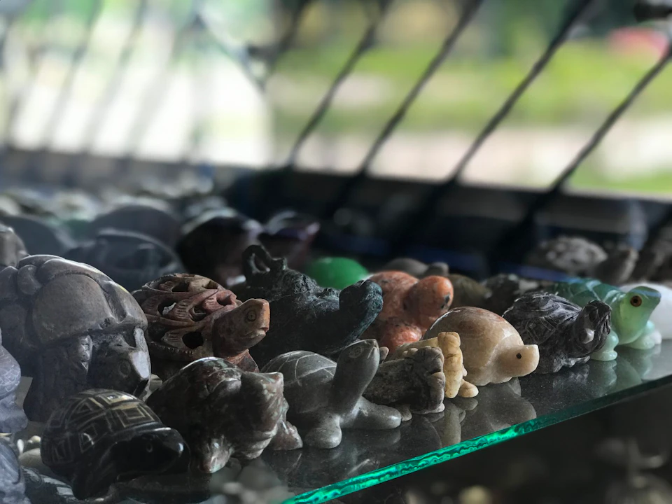 A collection of small turtle figurines made of various materials displayed on a glass surface with a blurred background.