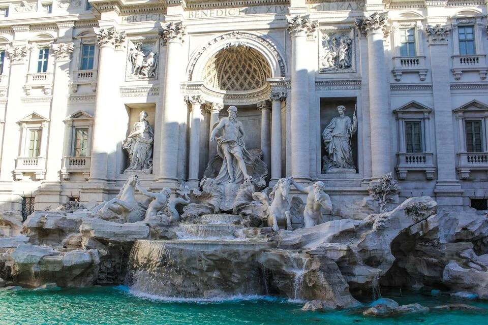 Detailed sculptures on the facade of a historical building, featuring a central figure and horses, above a turquoise fountain.